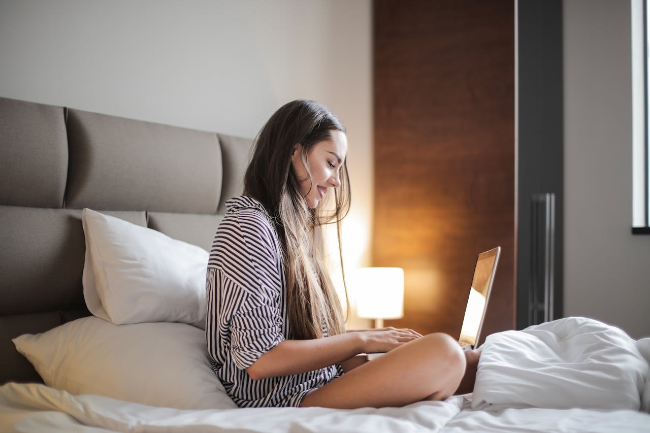 Young woman enjoying leisure time on her laptop in a comfortable bedroom environment.