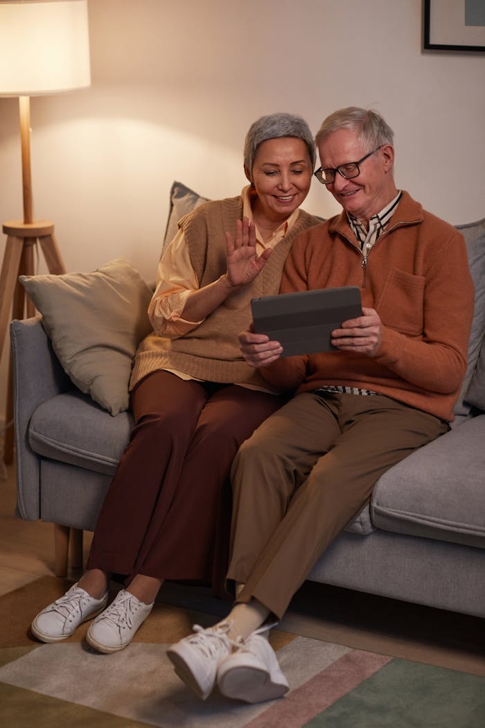 Happy senior couple sitting on a sofa enjoying a video call on a tablet together indoors.